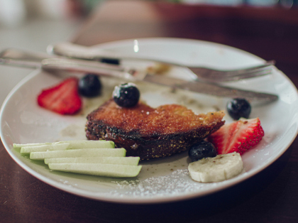 A white plate topped with french toast, bananas, strawberries, and blueberries.
