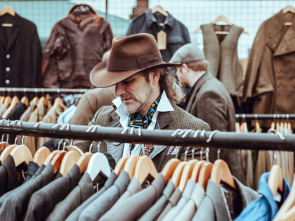 A man in a hat is looking at a rack of clothes.