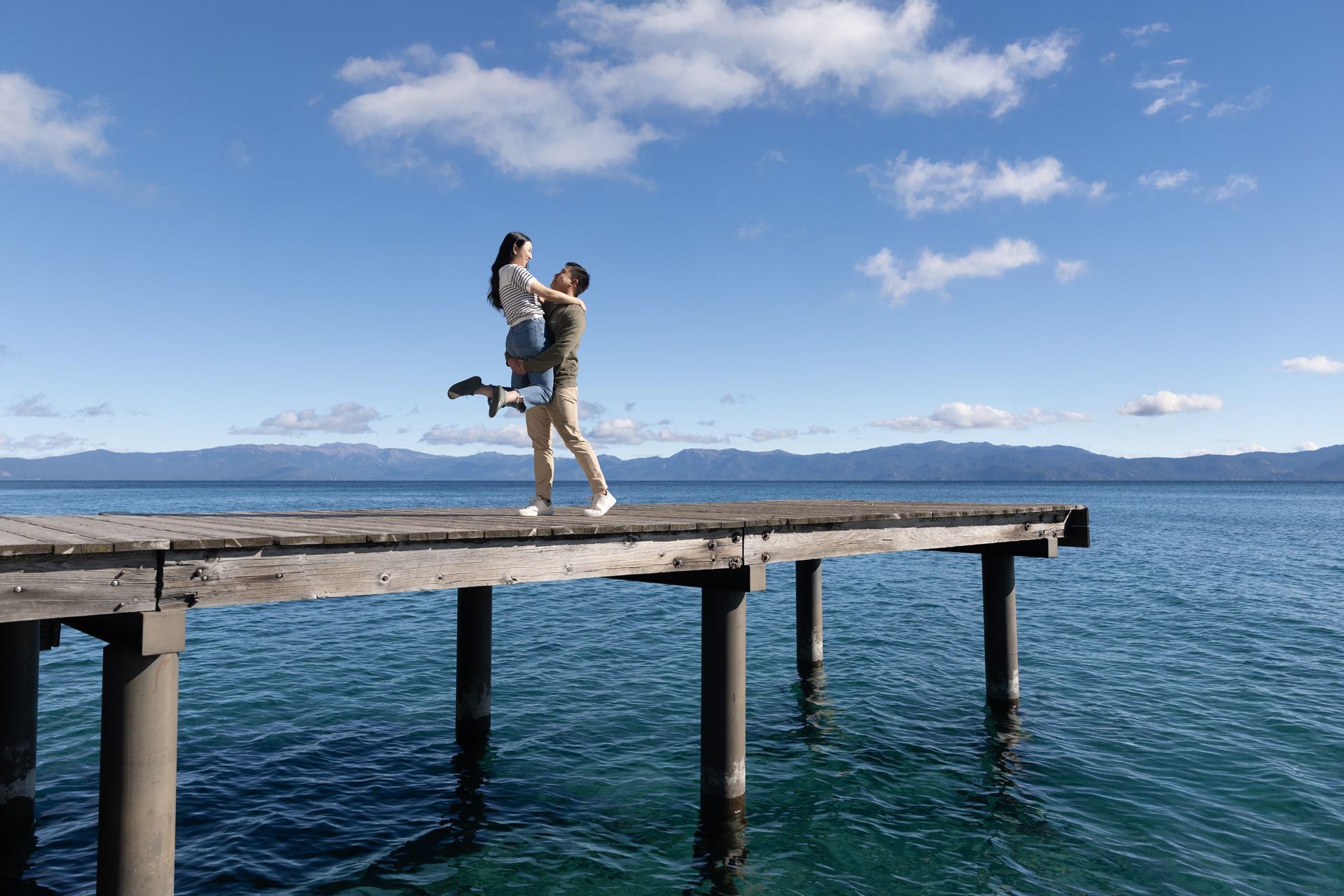 Photographer capturing a surprise engagement at Lake Tahoe with mountains and pine trees in the background.