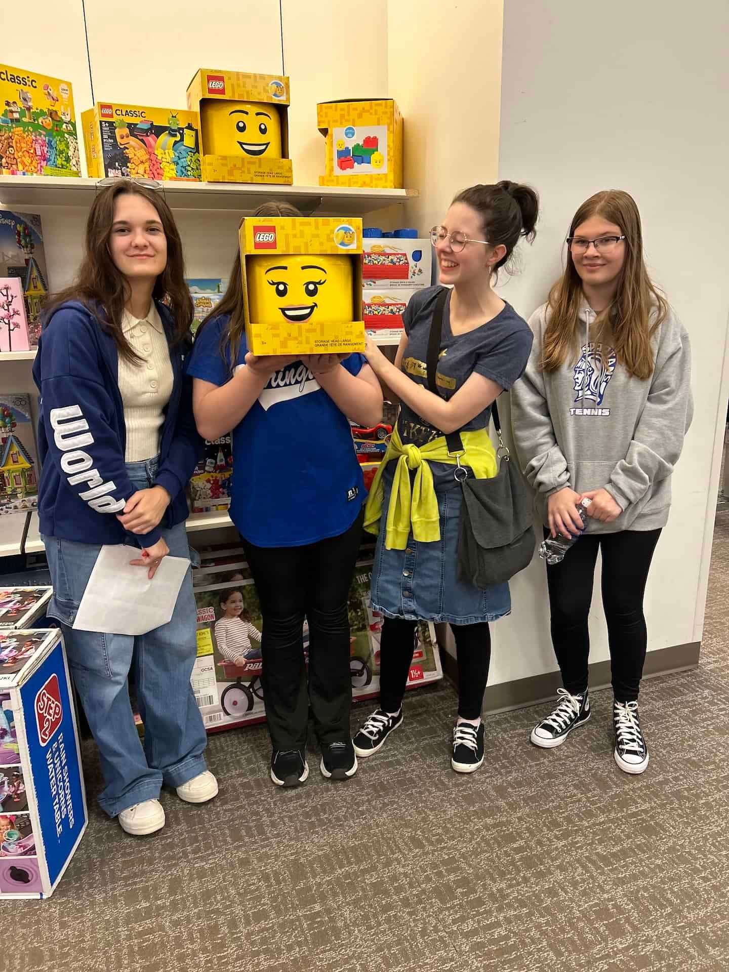 A group of girls are standing next to each other in a room holding a lego head.