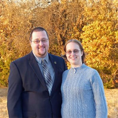 A man in a suit and tie is standing next to a woman in a sweater.