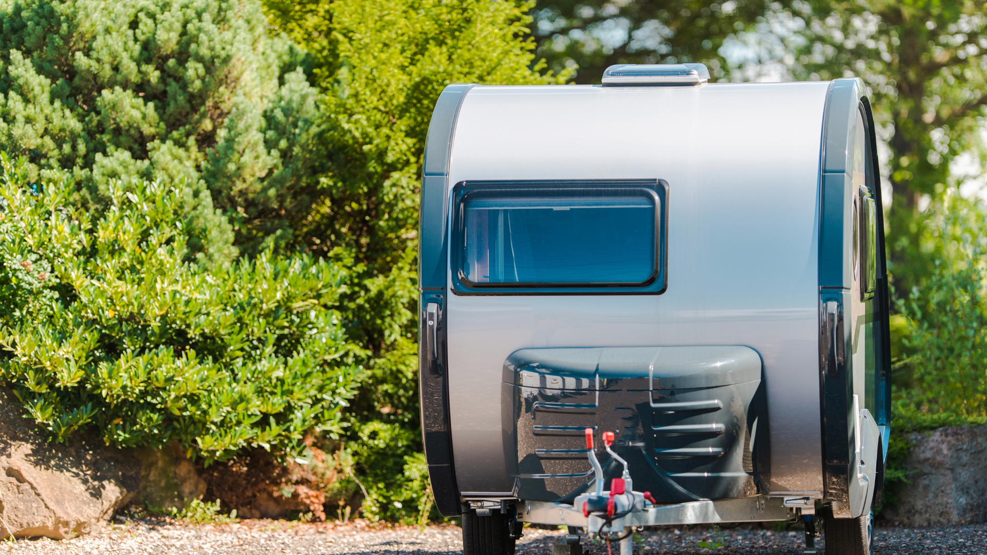 A person wearing blue gloves and jeans pressure washes the roof of a white RV on a sunny day.