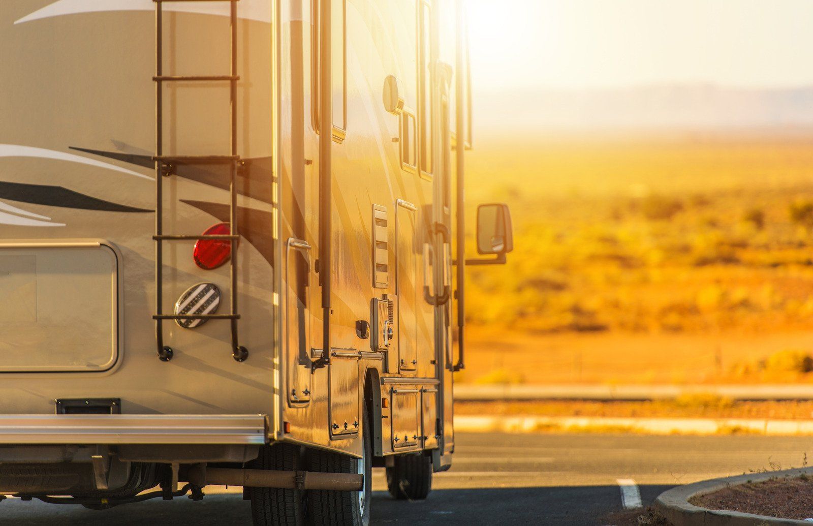 RV parked on a desert road at sunset; golden light illuminates the vehicle and landscape.