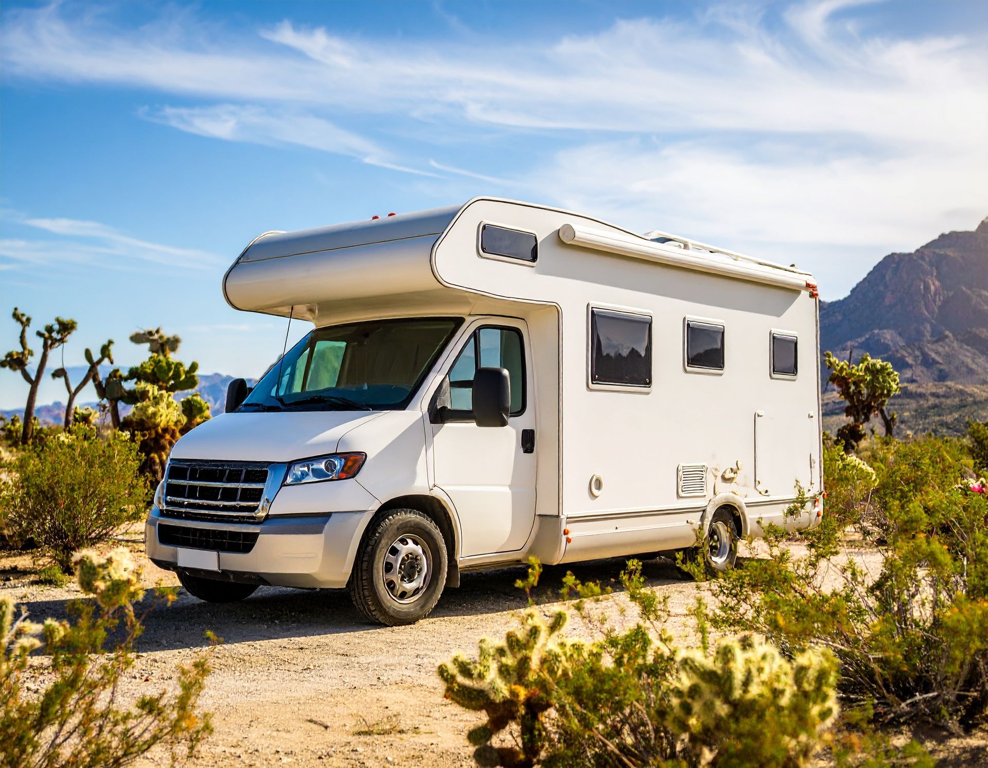 White RV parked on a dirt road in a desert landscape, with cacti and mountains in the background.