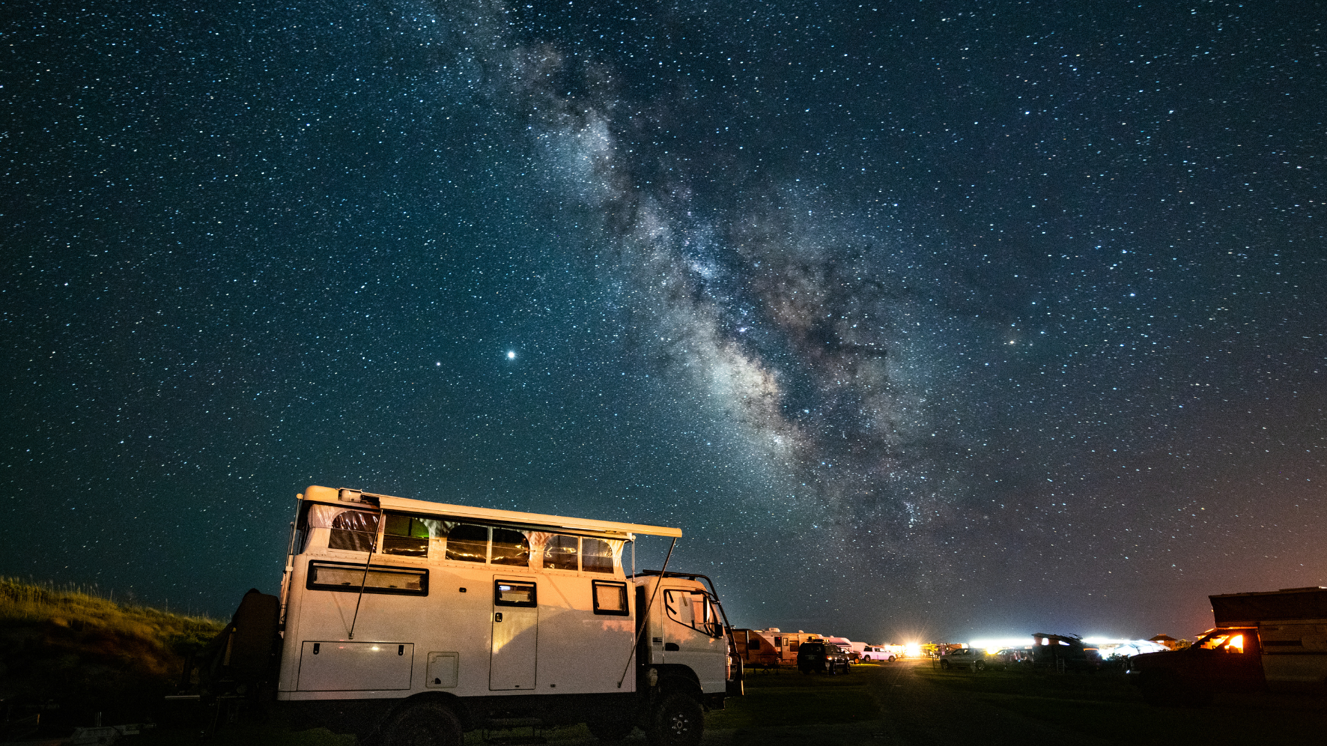 Milky Way galaxy shining above a white, weathered truck in a dark field at night.