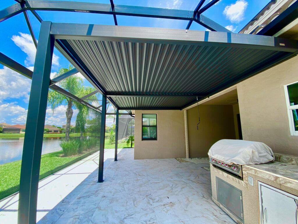 Dark gray pergola over a patio next to a house with a view of a lake and a screened enclosure.