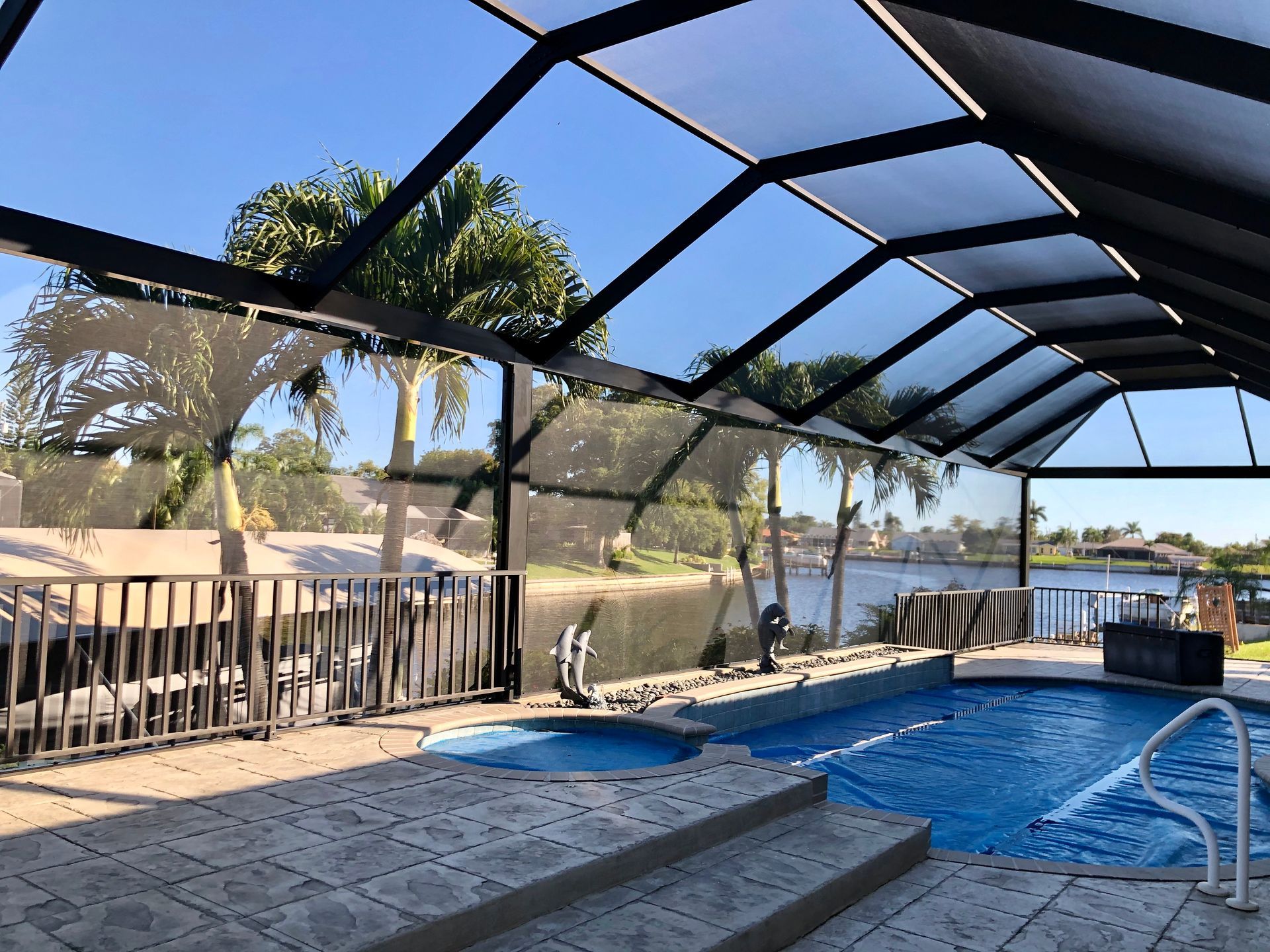 Gray pergola with fireplace and seating on a stone patio, surrounded by landscaping and urn fountains.