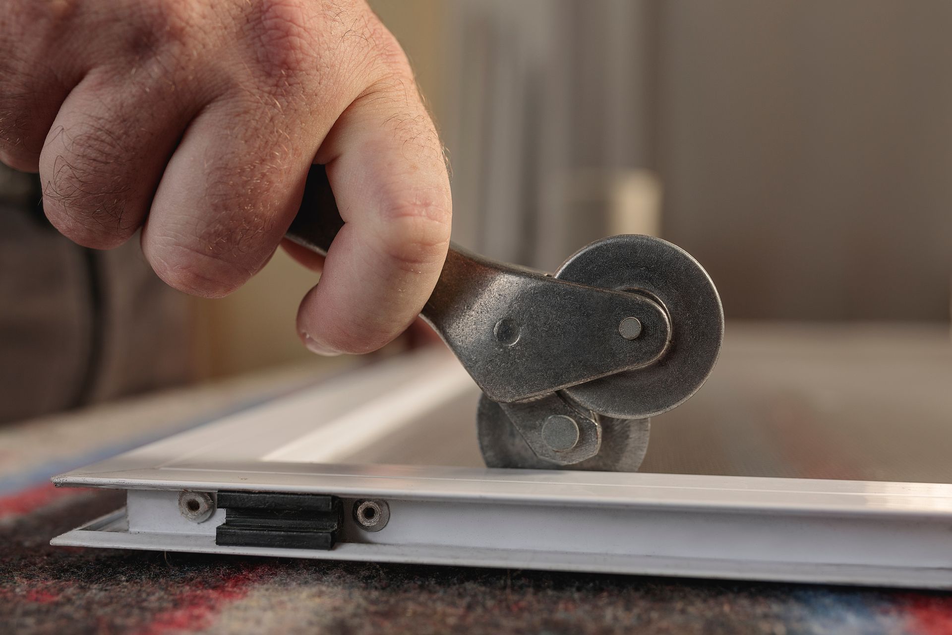 Hand using a screen roller to install screen mesh in a window frame.
