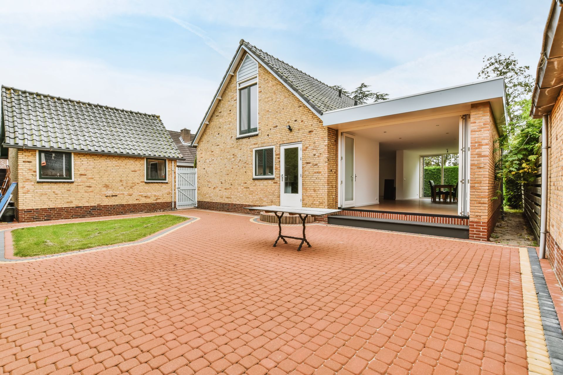 Brick-paved patio of a yellow brick house with a covered outdoor area and a smaller brick building.