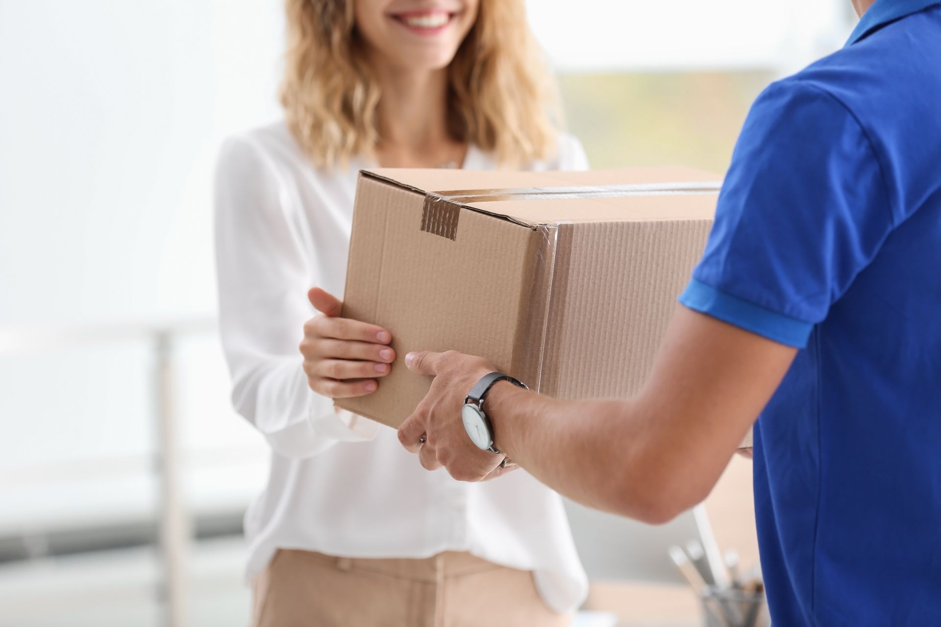 Delivery person handing a cardboard box to a smiling person indoors