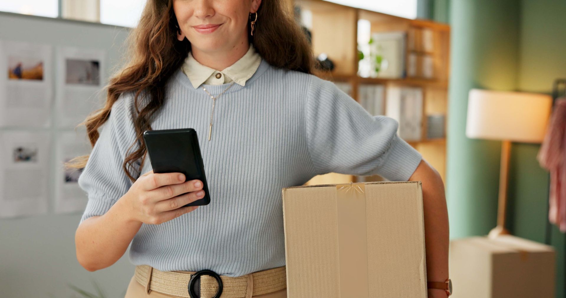 Woman smiling, holding phone and cardboard box
