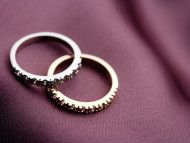 Two wedding rings, silver and gold, interlocked on a purple satin fabric.