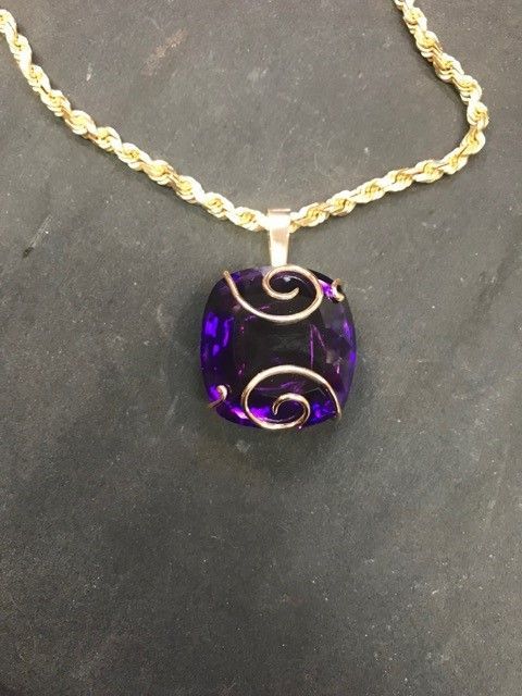 Purple square pendant with spiral silver design on gold chain.
