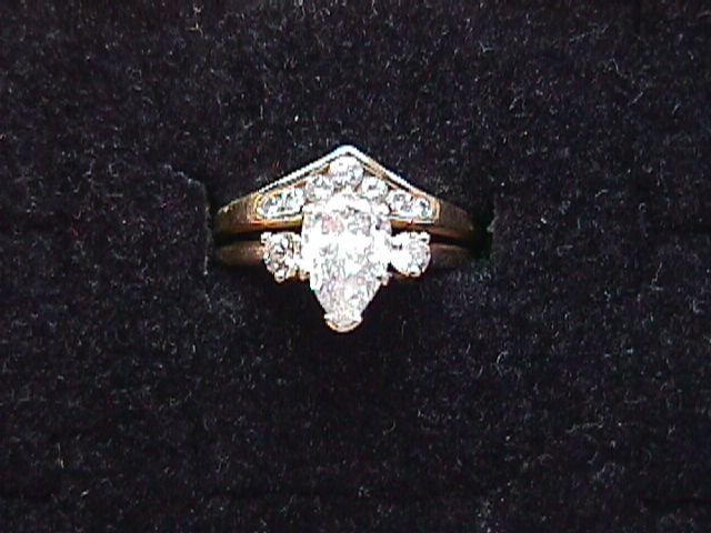 Gold ring set with pear-shaped center diamond and smaller diamonds on a black background.