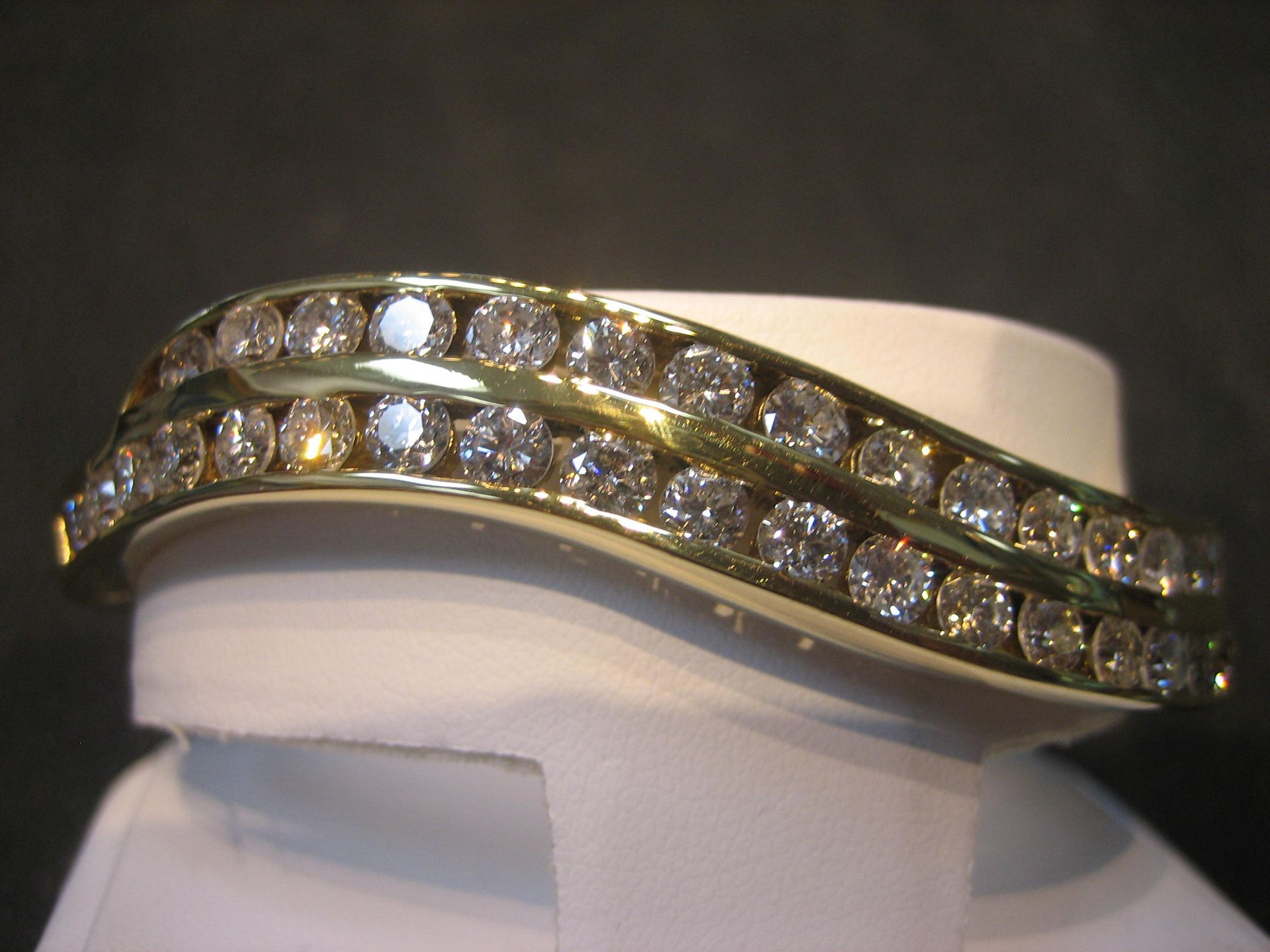 Diamond and gold bracelet on a white stand. The bracelet curves with rows of diamonds.