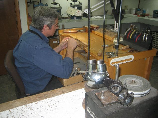 Man working at a workbench, focused on jewelry repair. Tools and equipment visible in a workshop setting.