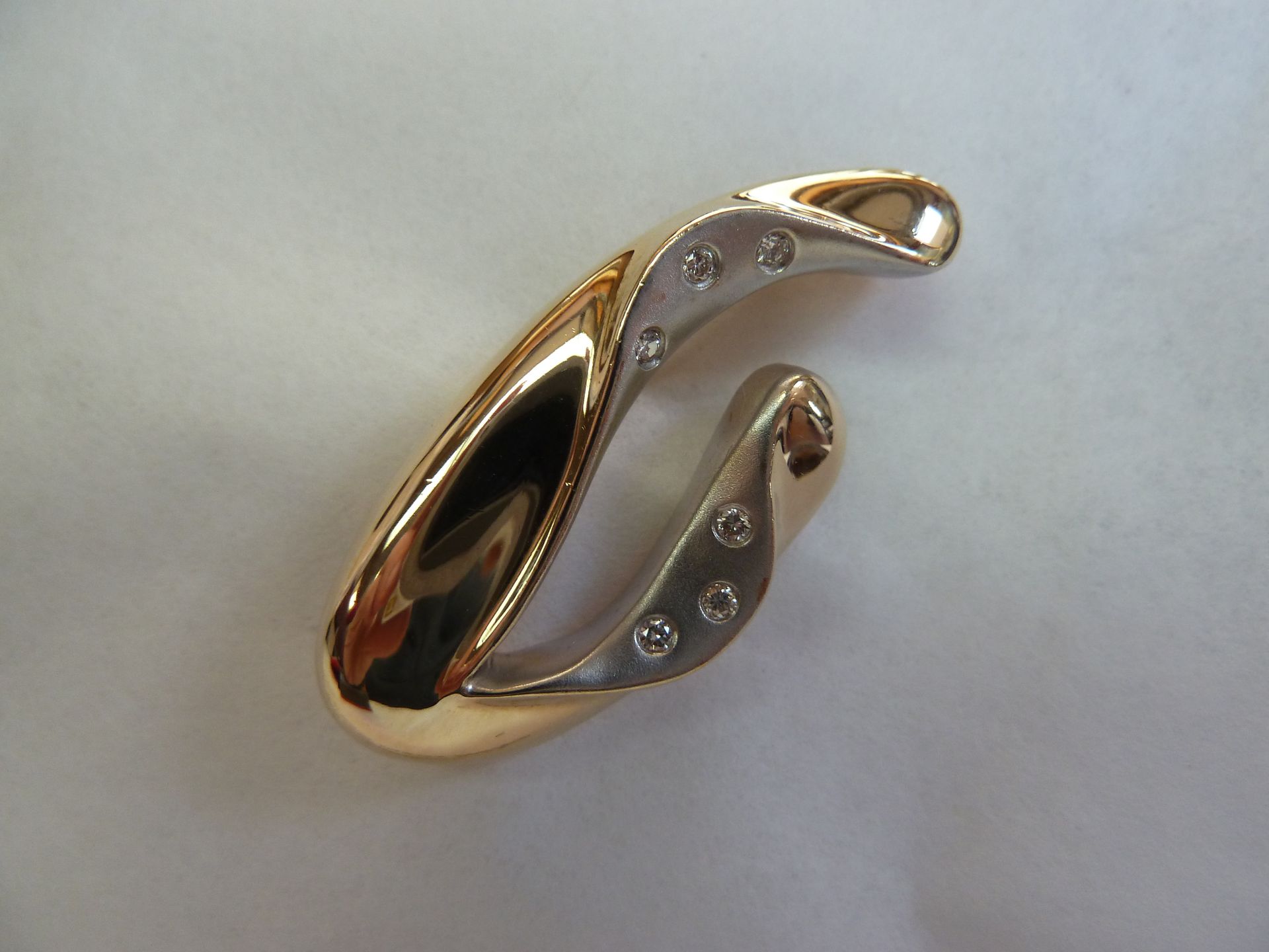 Gold and silver pendant with embedded diamonds in a curved design.