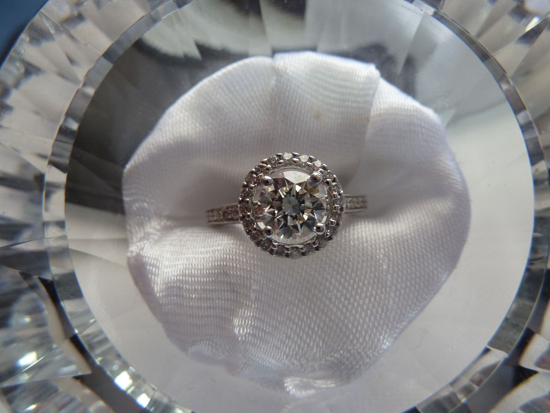 Diamond engagement ring on white fabric, displayed in a clear glass bowl.