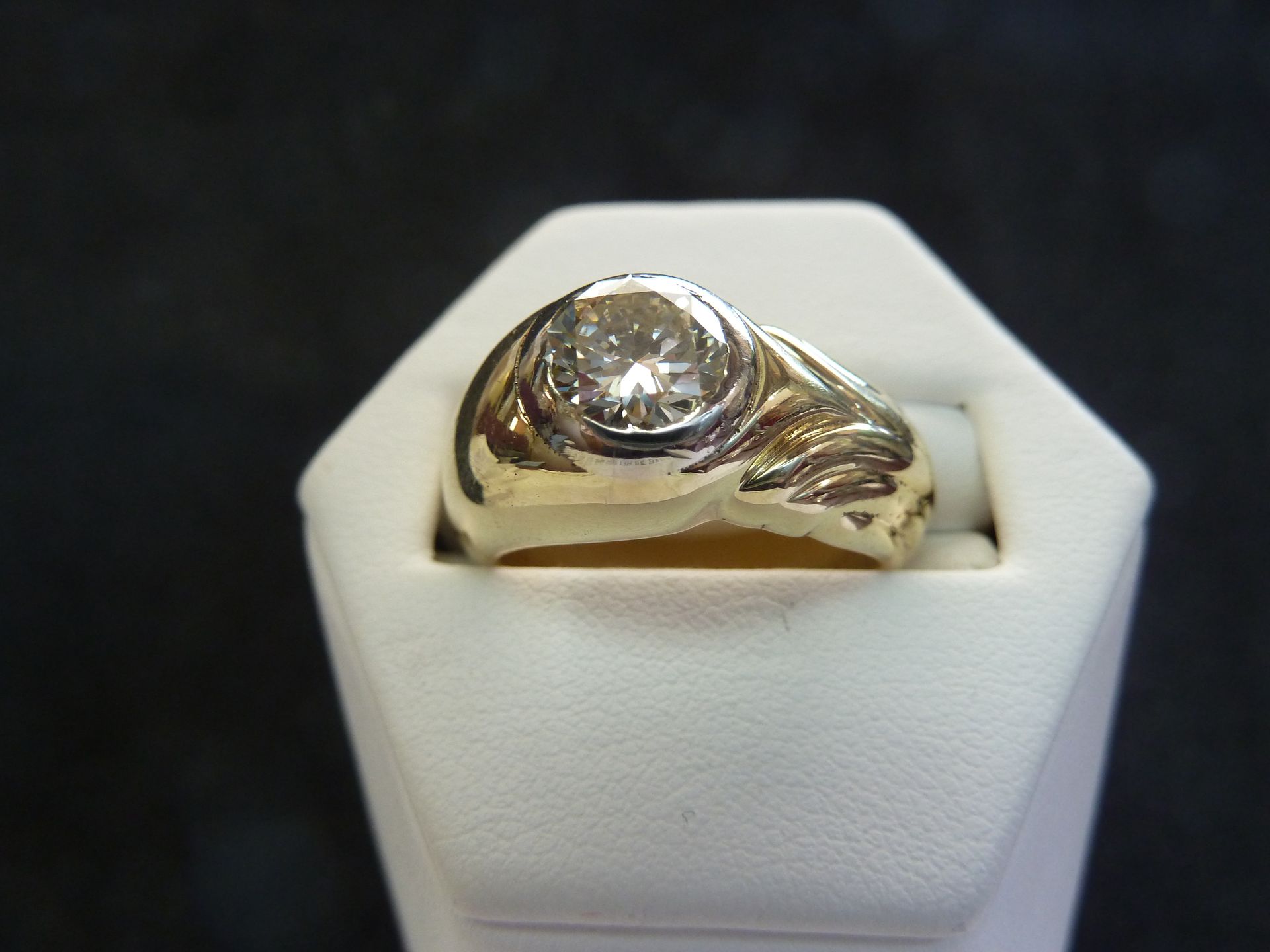 Gold ring with a large, clear gemstone on a white display stand.