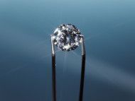 Diamond held by tweezers against a blue background, reflecting light.