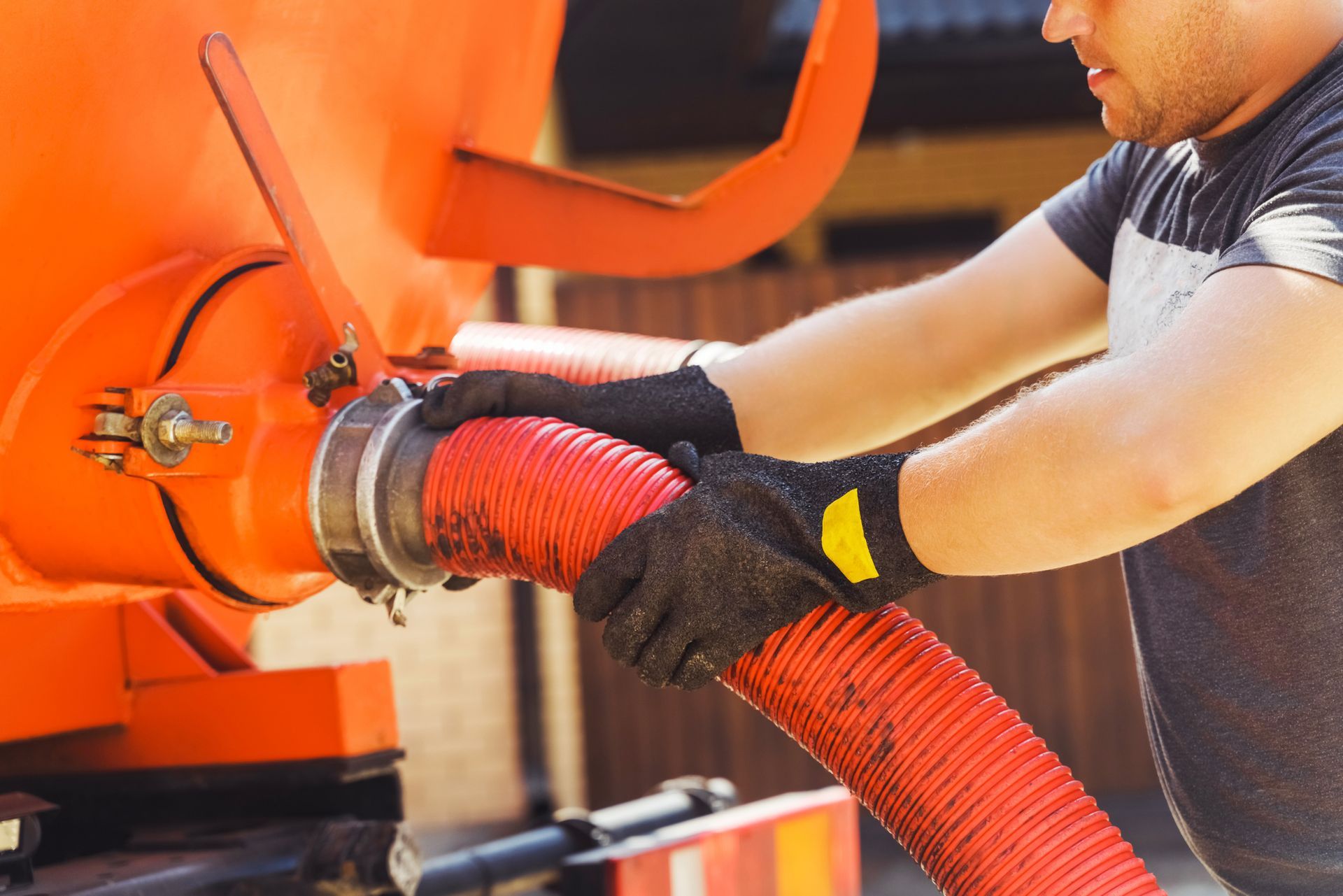Man in gloves connecting a red hose to an orange tank.