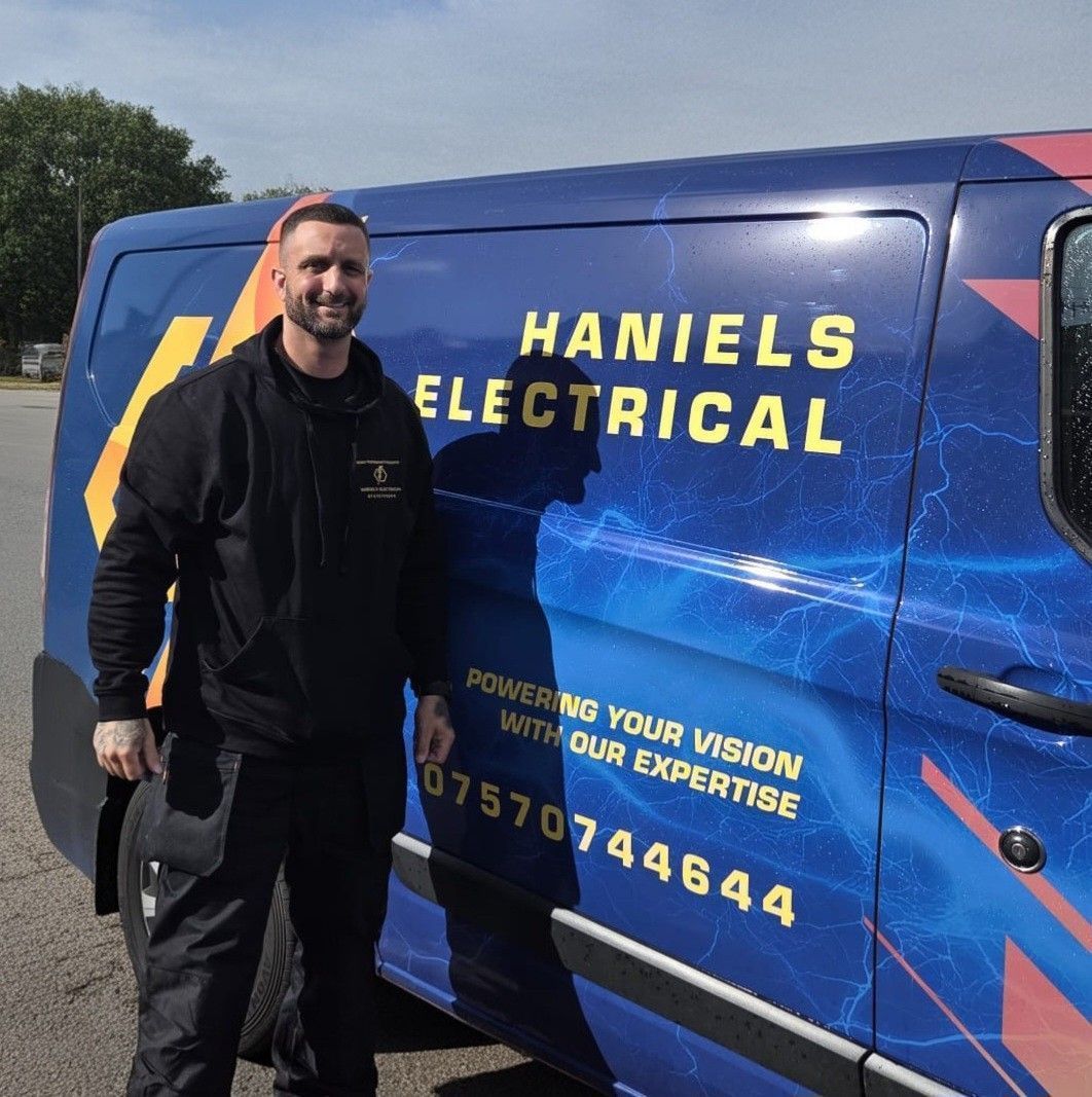 A person stands beside a blue Haniels Electrical work van with their phone number displayed on the side.