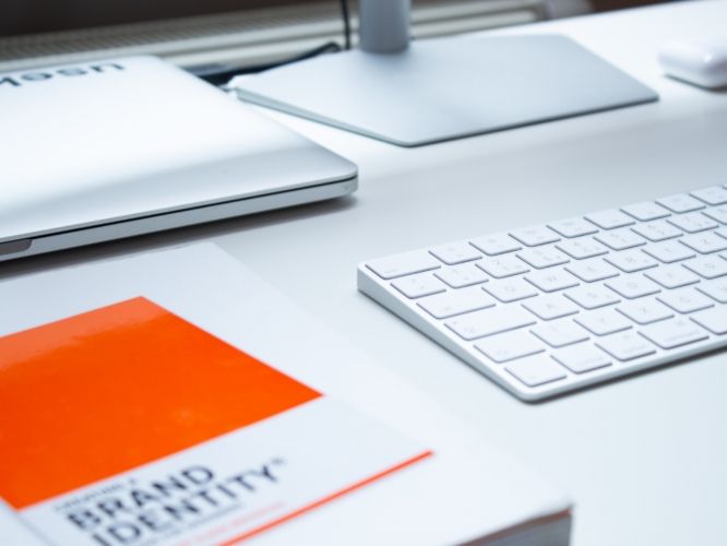 White desk with a laptop, keyboard, monitor, and a book titled 