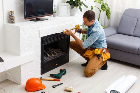 A man is kneeling down in a living room fixing a fireplace.