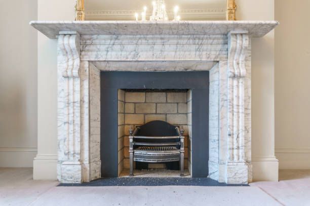 A fireplace with a marble mantle and a black grate in a living room.