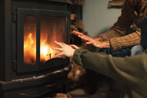A man and a woman are warming their hands in front of a fireplace.