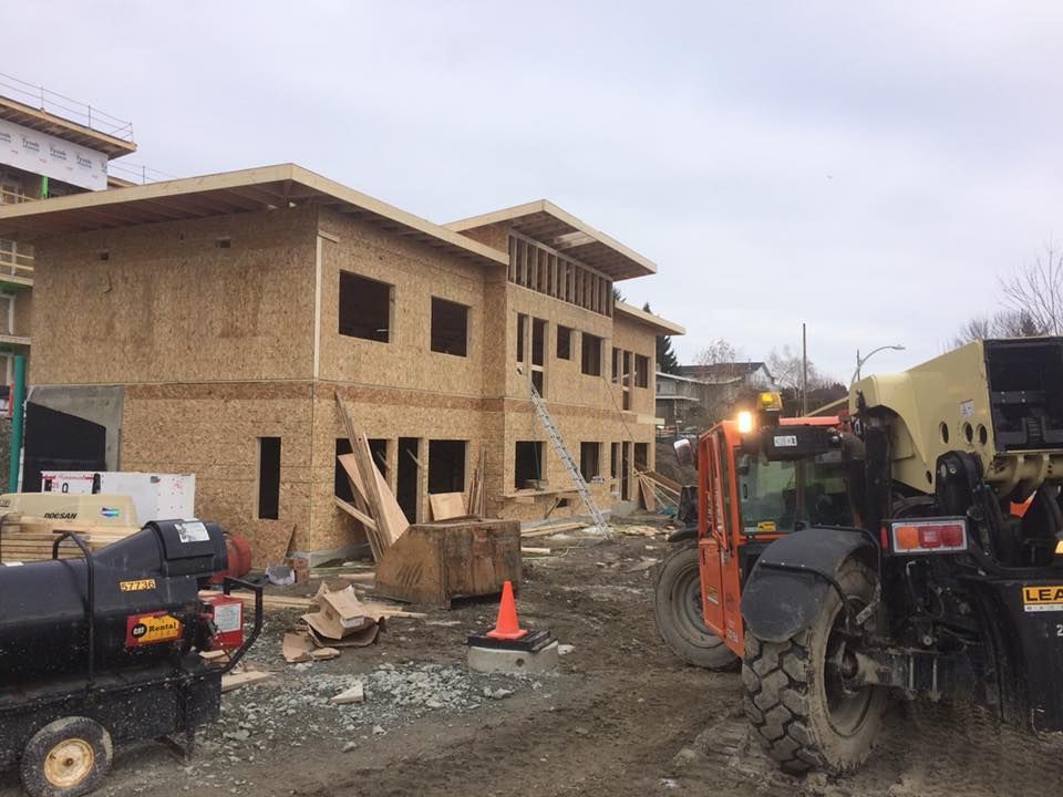 Construction site with wood-framed building, a forklift, and ground-level dirt. Overcast day.