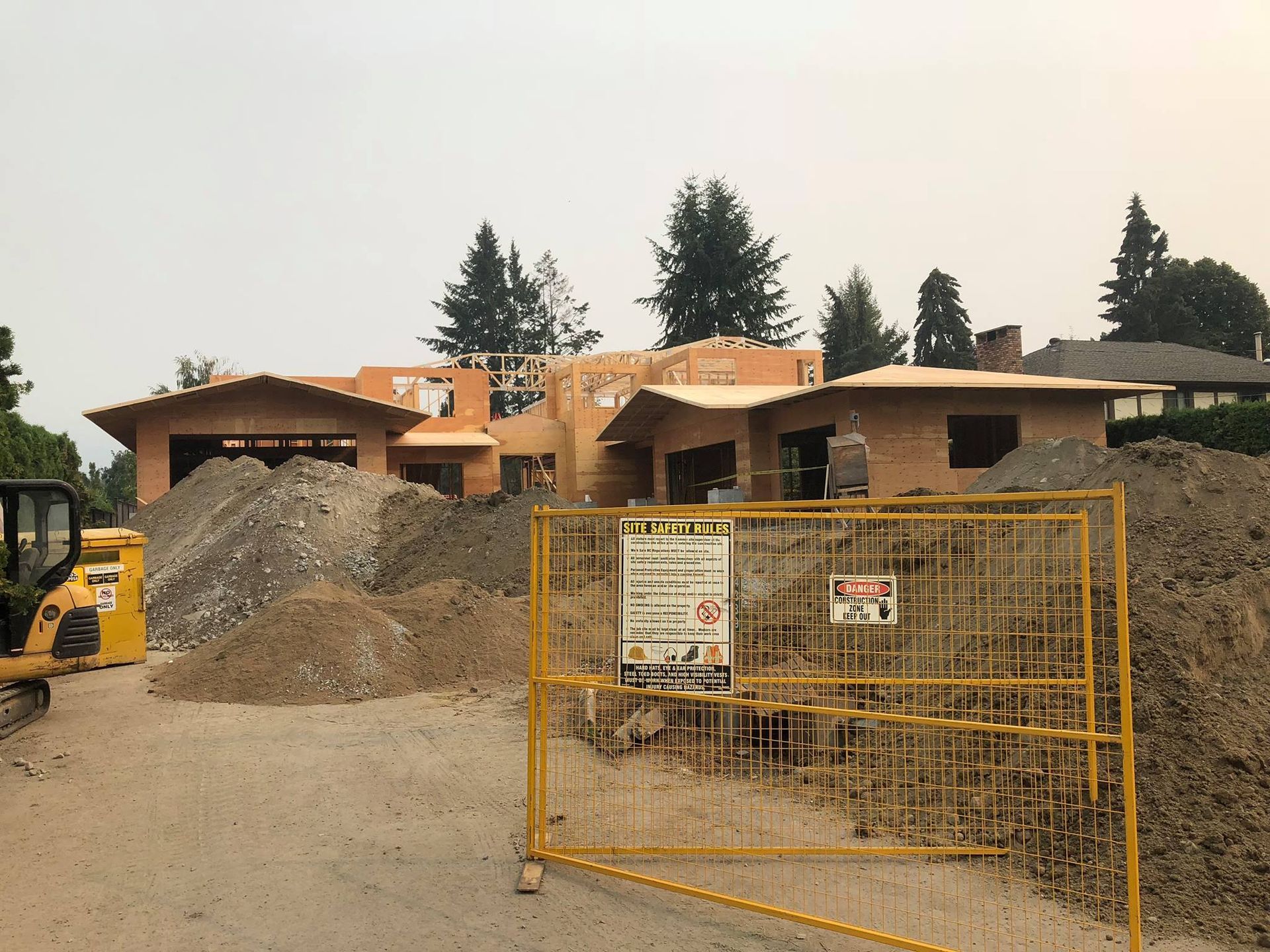 Construction site with a partially built brick house, piles of dirt, and yellow safety fence.