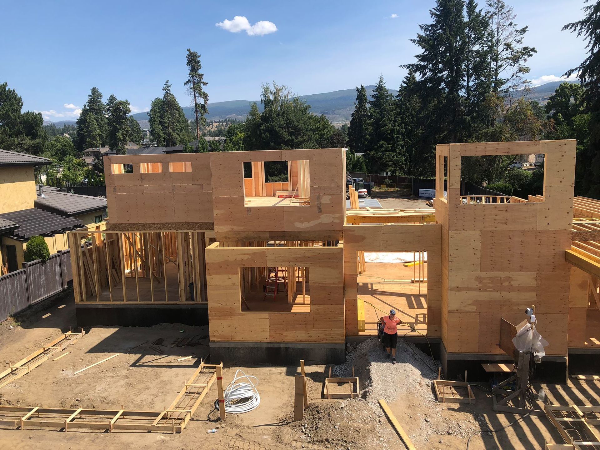 House under construction, wood framing, a worker visible. Bright sunny day.