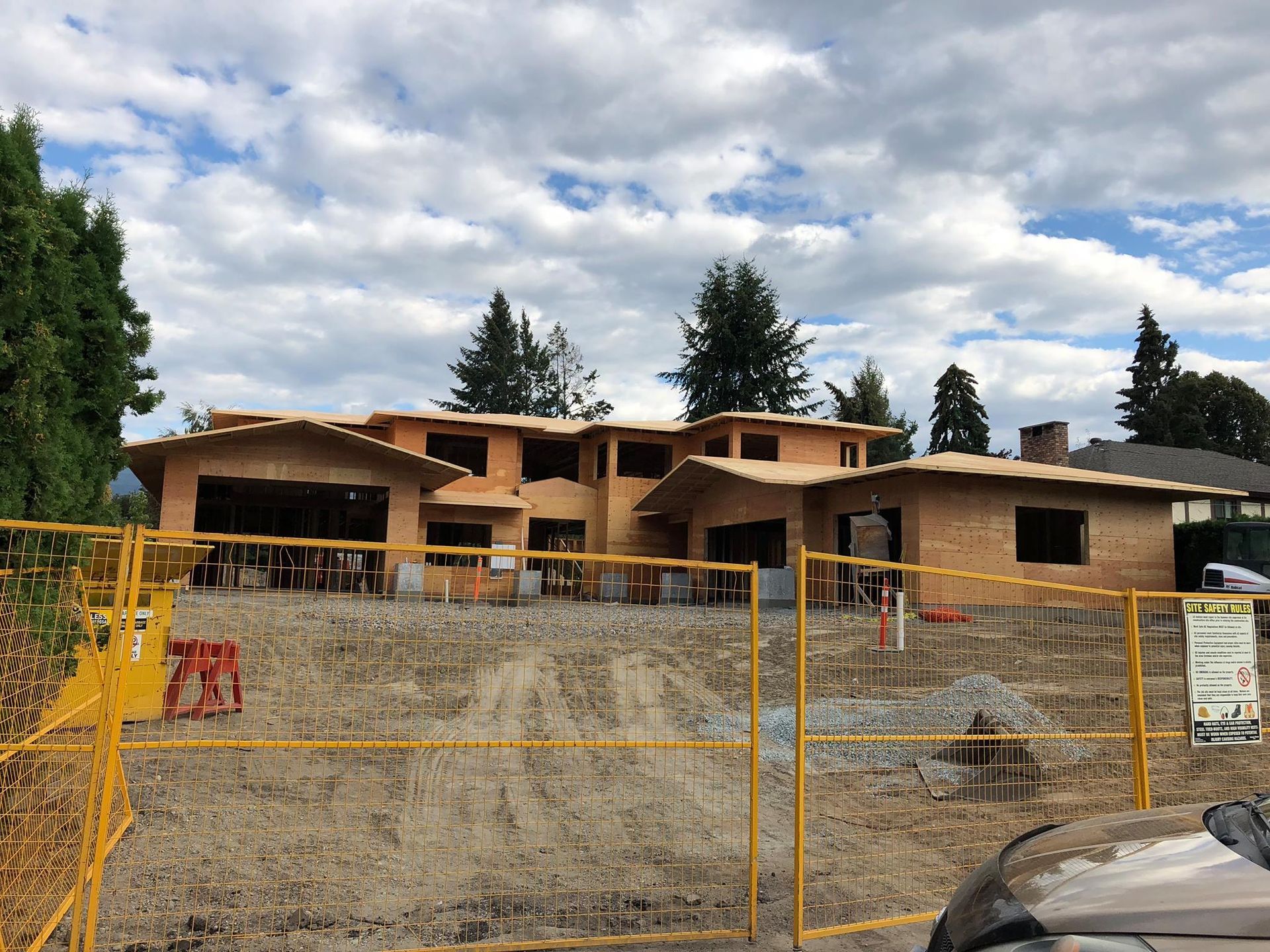 Construction site with exposed wooden framing; yellow fencing, cloudy sky.
