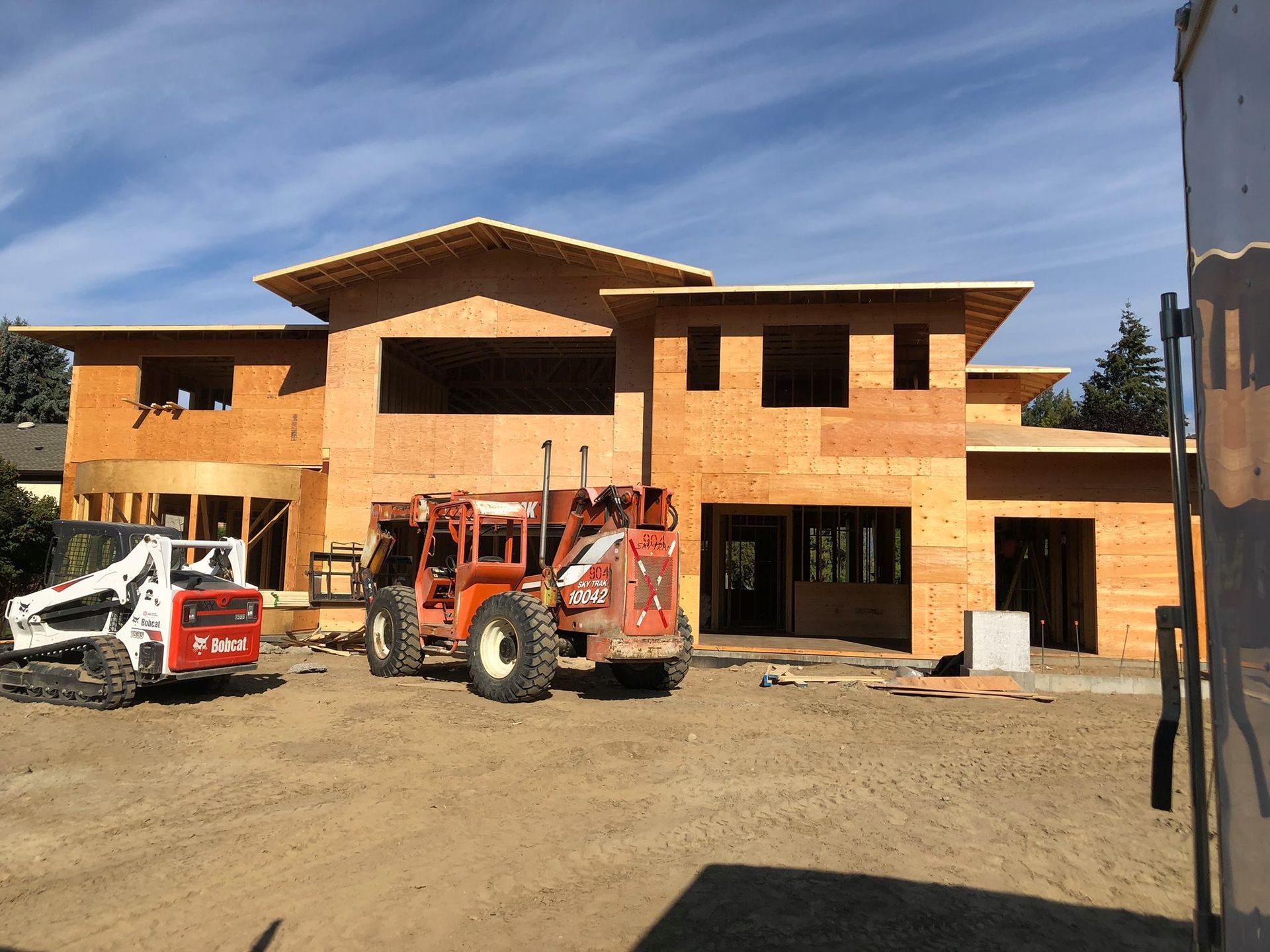 Construction site with a wooden house frame, heavy machinery, and clear sky.