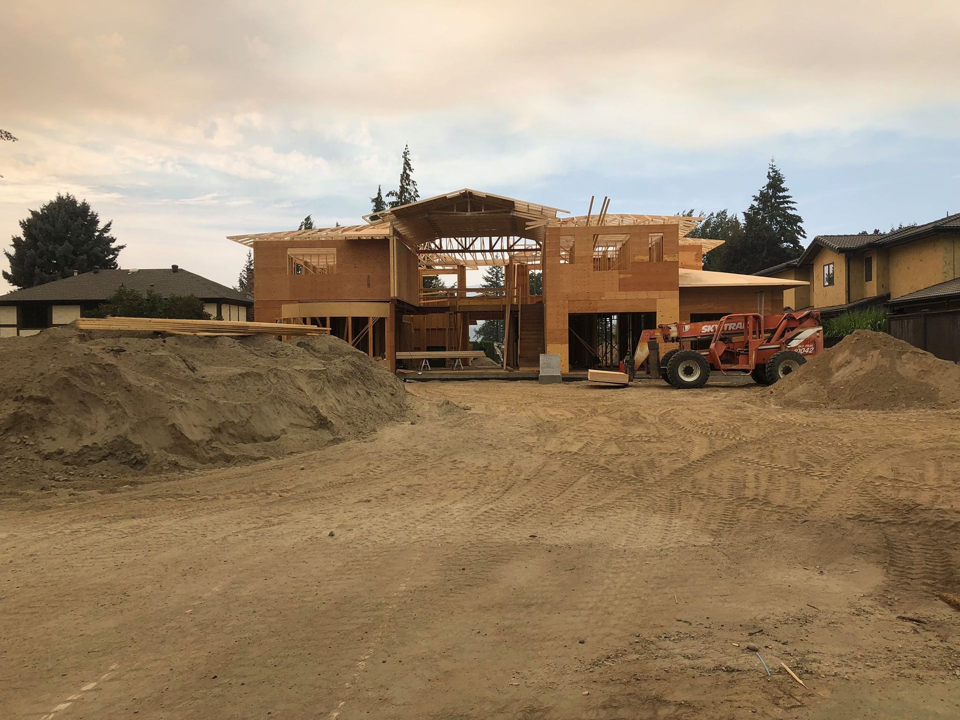 House under construction, wooden frame, surrounded by dirt piles and equipment.