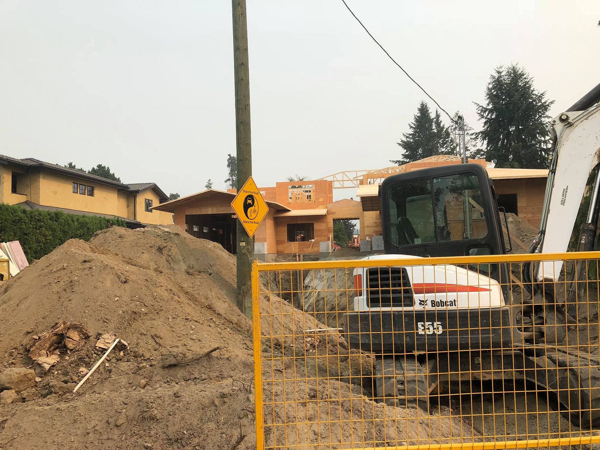 Construction site with excavator, pile of dirt, and sign warning of falling objects.