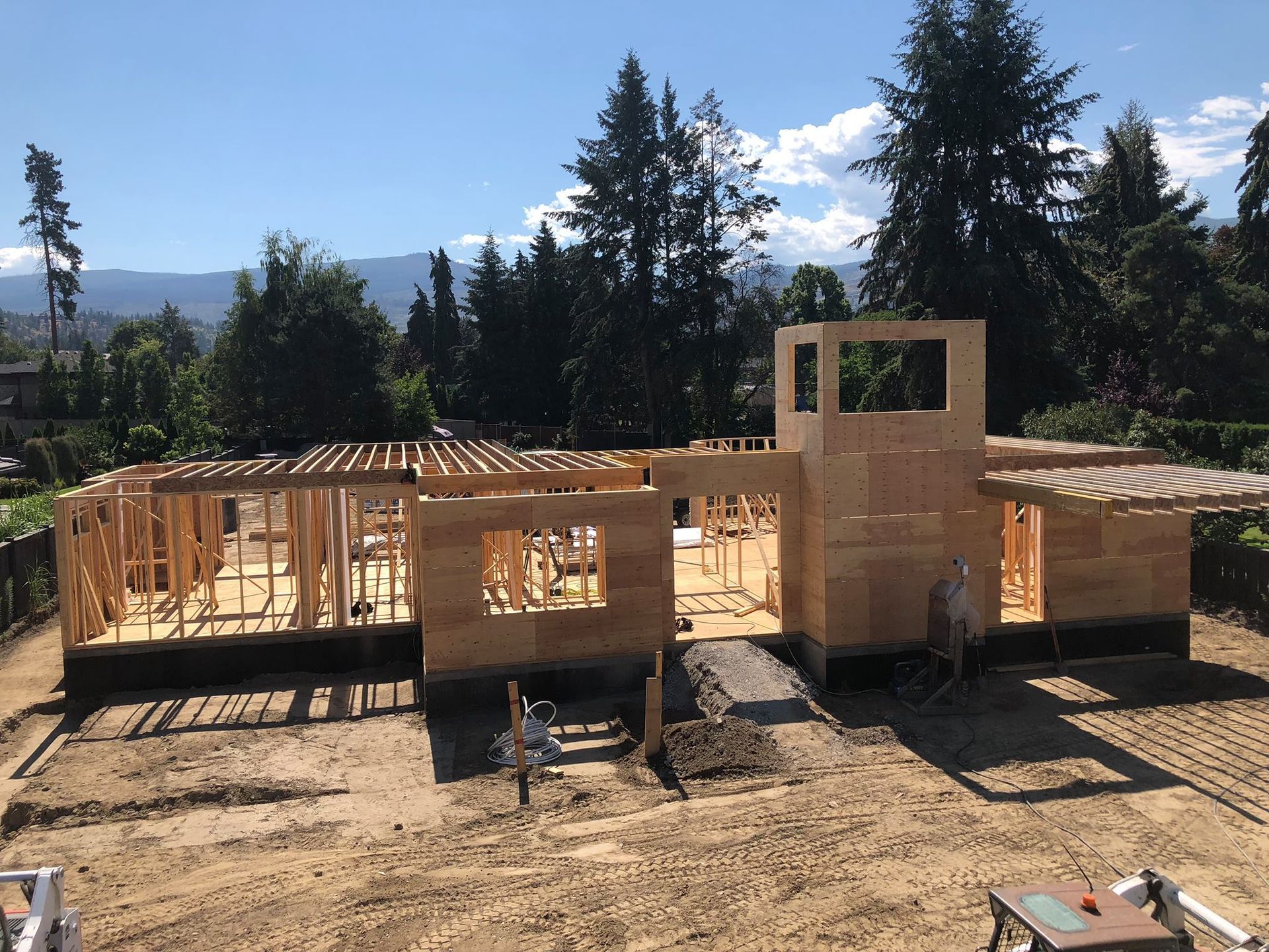 Construction site with wooden framing of a single-story house under a blue sky.