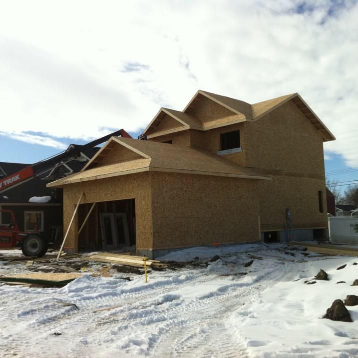 House under construction, wood frame, snow on the ground, blue sky in the background.