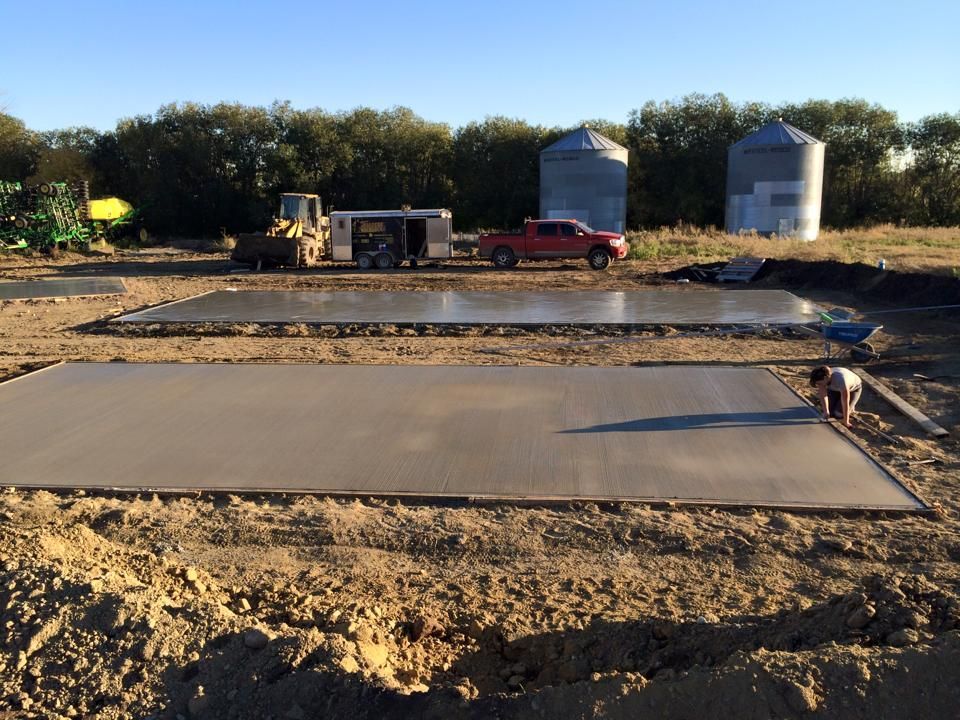 Two rectangular concrete pads, one with a person, outdoors near grain silos and a red truck.