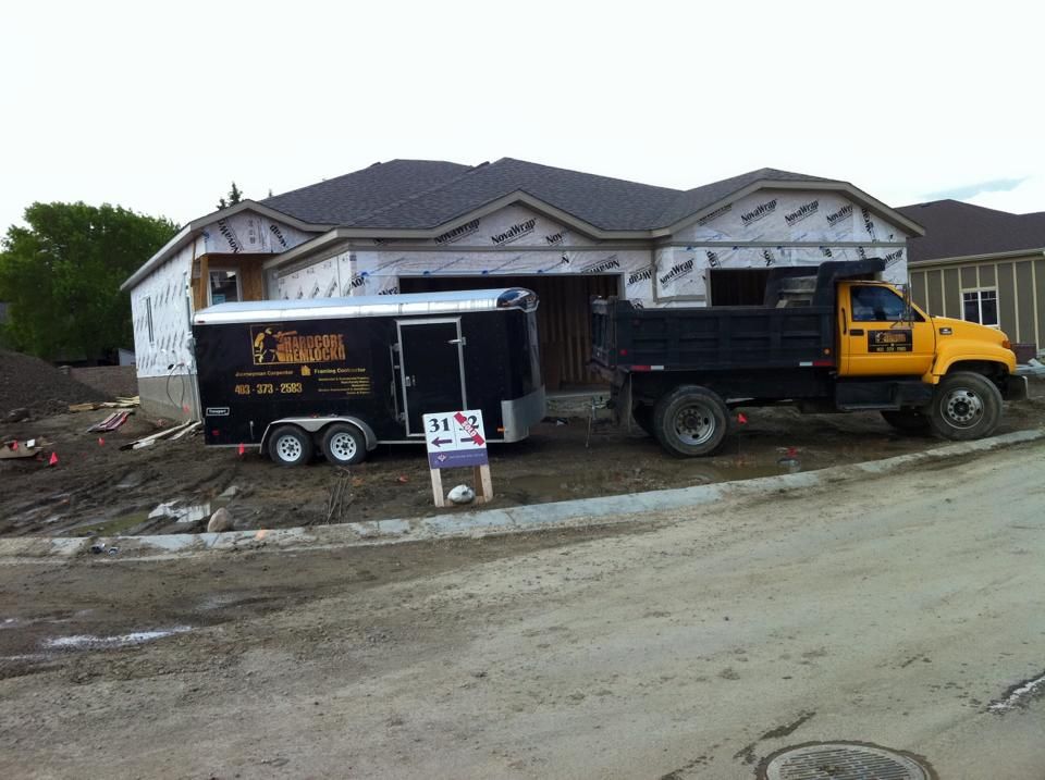 Construction site: Black trailer and yellow dump truck in front of a house under construction.