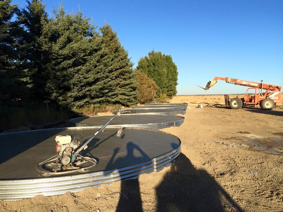 Concrete silos being constructed on a farm, with a power trowel in use. An orange forklift is nearby.