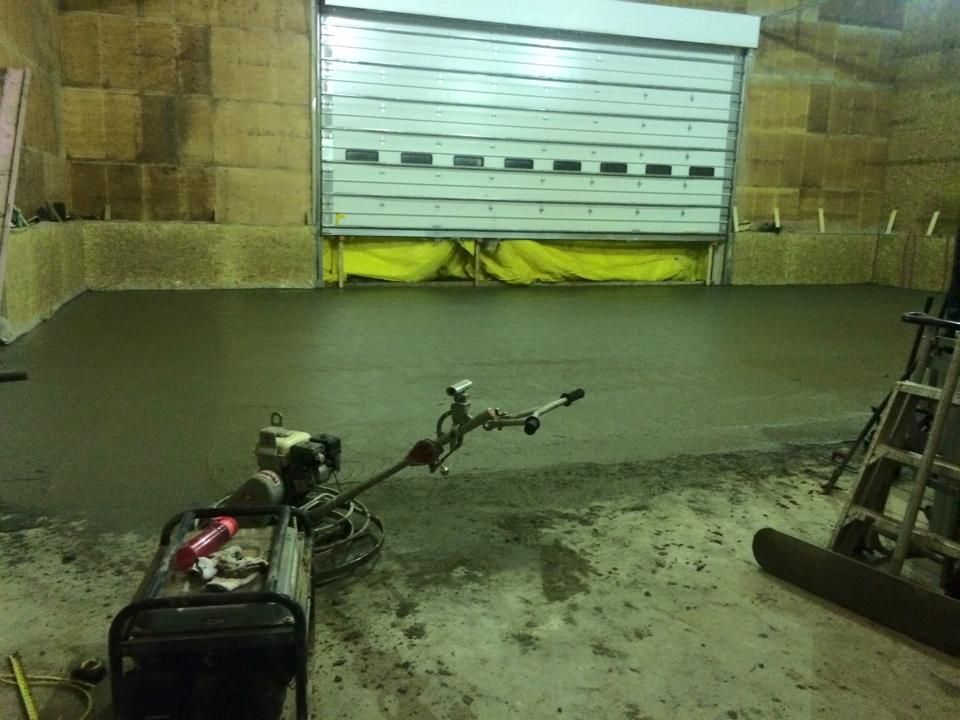 A freshly poured concrete floor in a warehouse with a garage door, finishing machine, and hay bale walls.