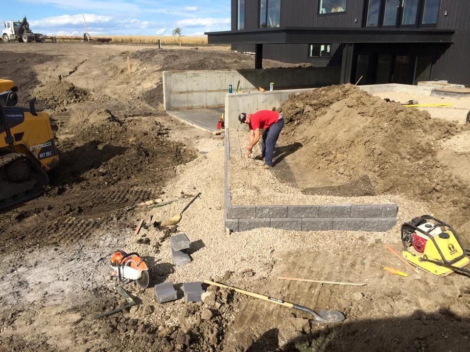 Construction worker building a retaining wall near a modern house with heavy machinery.