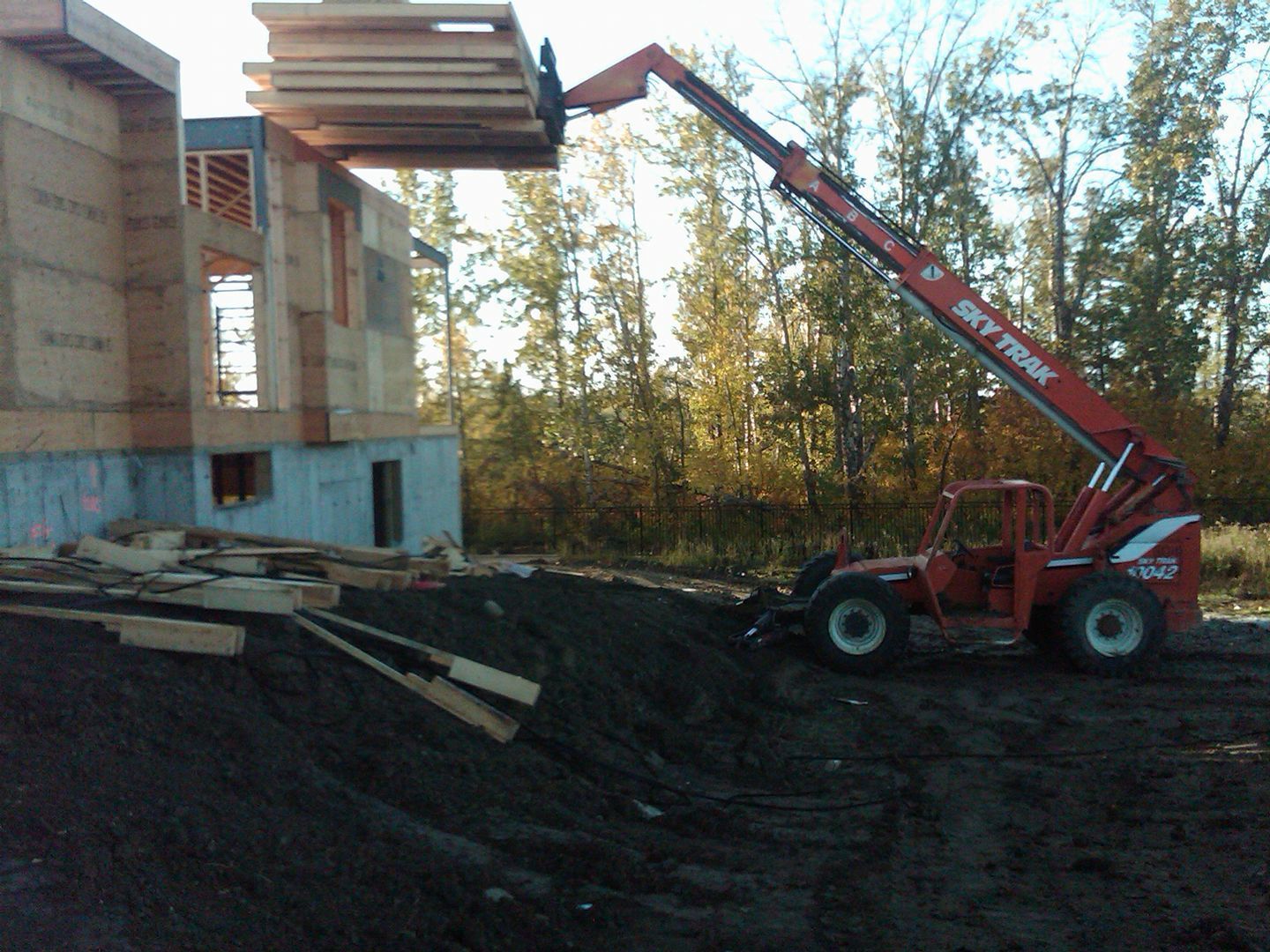 A telehandler lifting lumber to the upper level of a building under construction; outdoors.