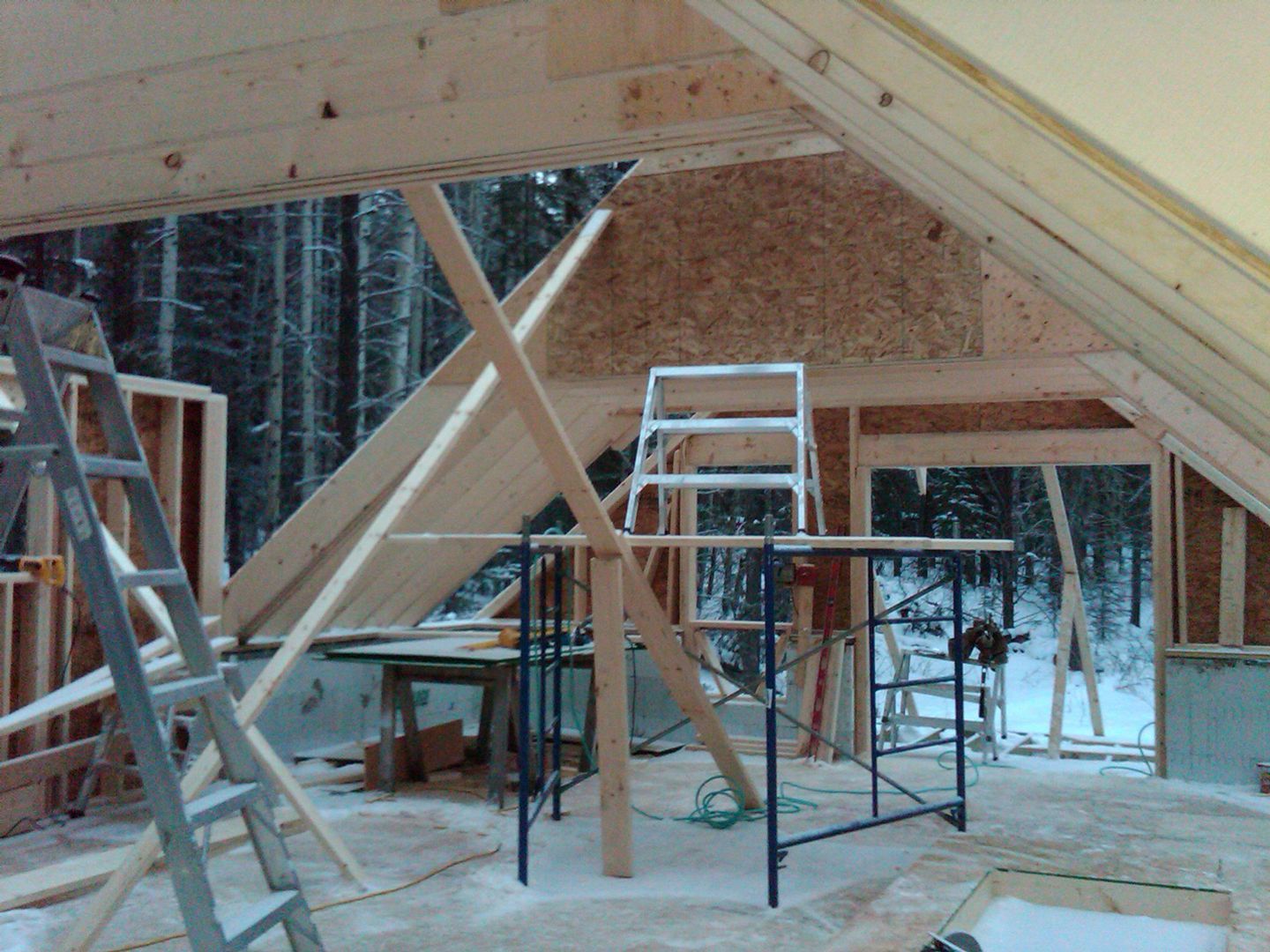 Interior of a wooden structure under construction, with ladders, scaffolding, and a snowy forest visible through an opening.