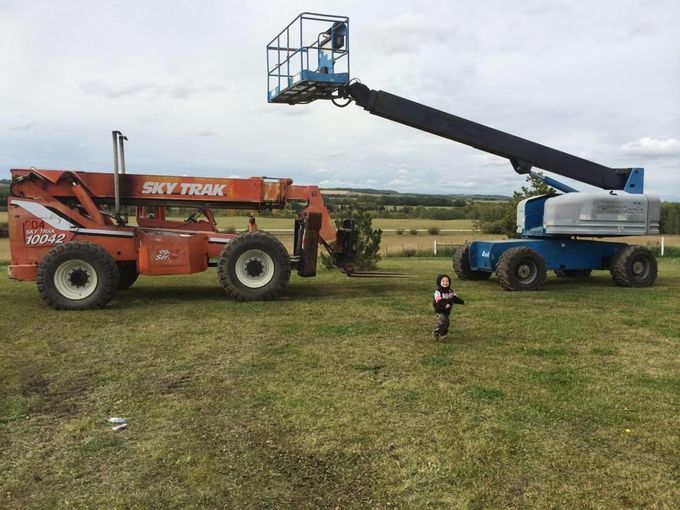 Orange Sky Trak and blue lift, child running on grass field, cloudy sky in background.