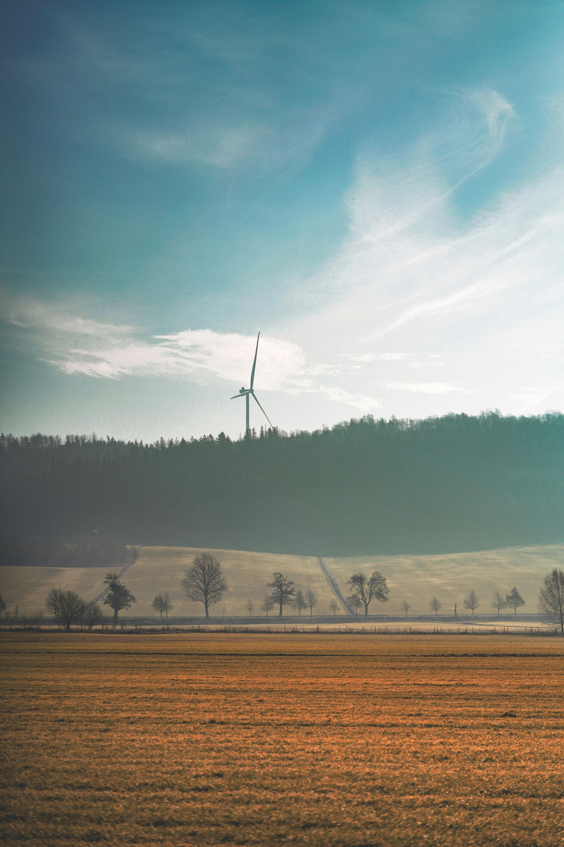 En vindmølle står på toppen af ​​en bakke midt på en mark.