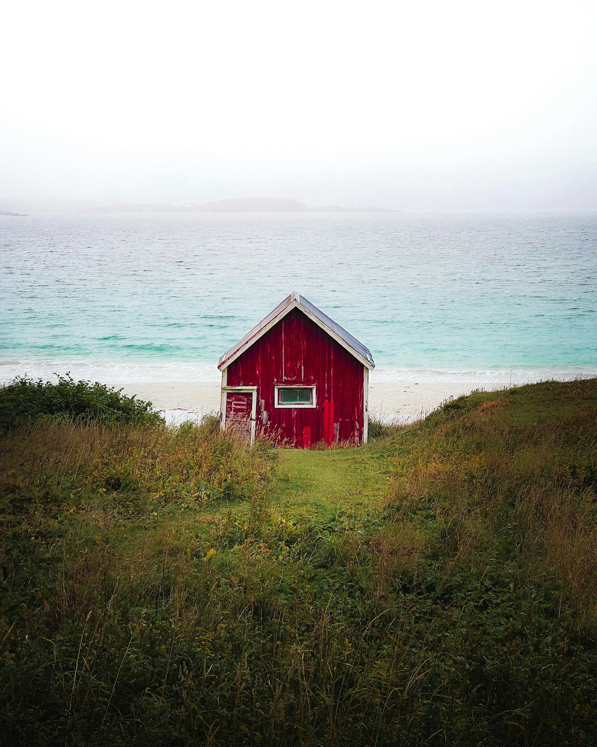 En rød lade sidder på toppen af ​​en græsklædt bakke ved siden af ​​havet.