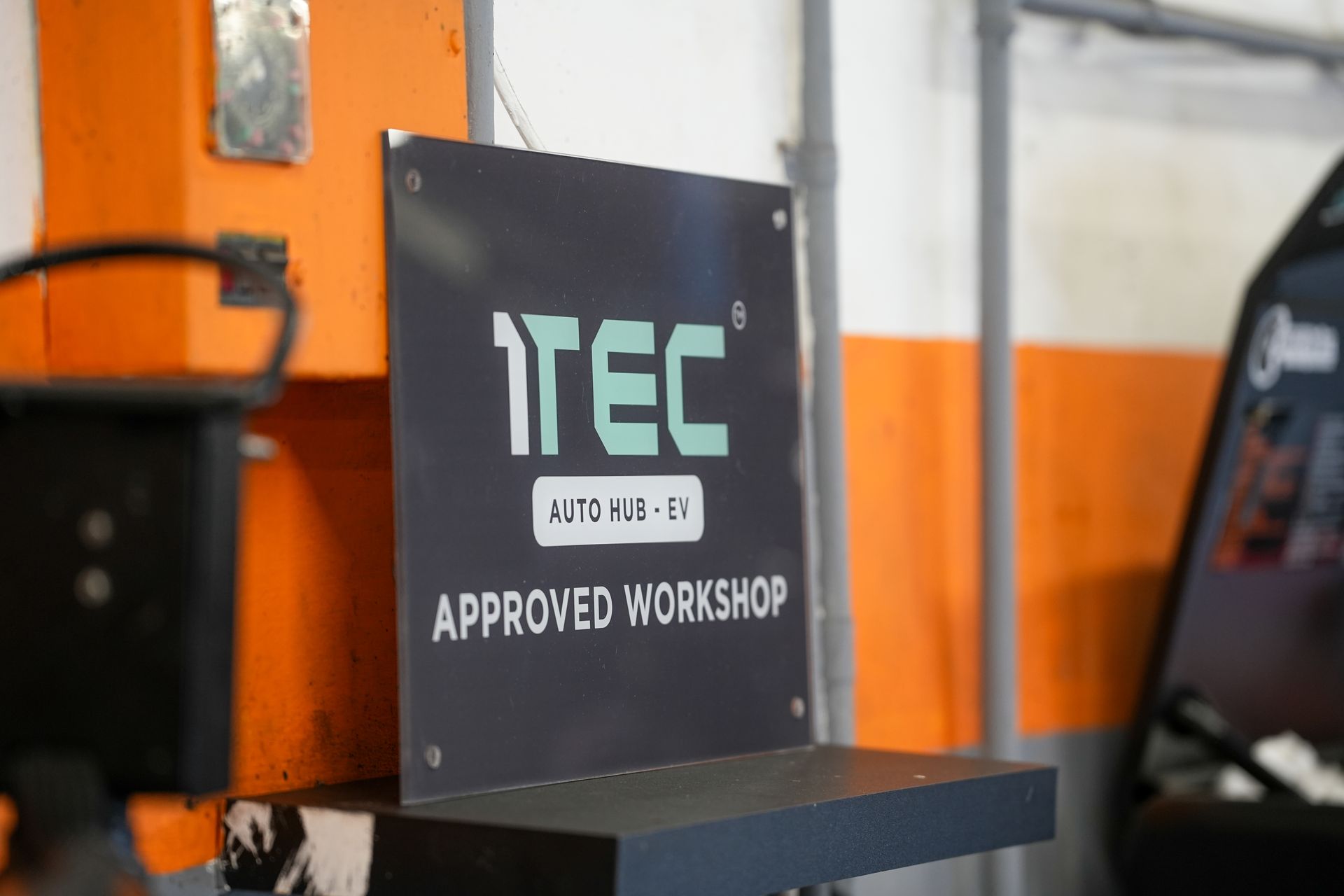 A person holding a handheld diagnostic scanner, reviewing the interface next to a black car in an automotive garage.